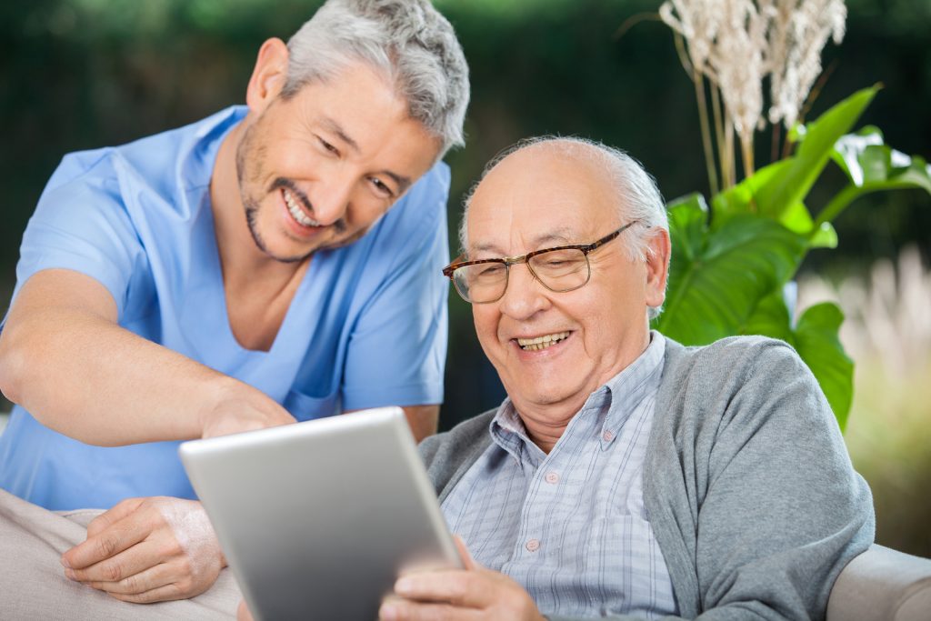 Happy male nurse and senior man enjoying while using tablet computer in nursing home porch