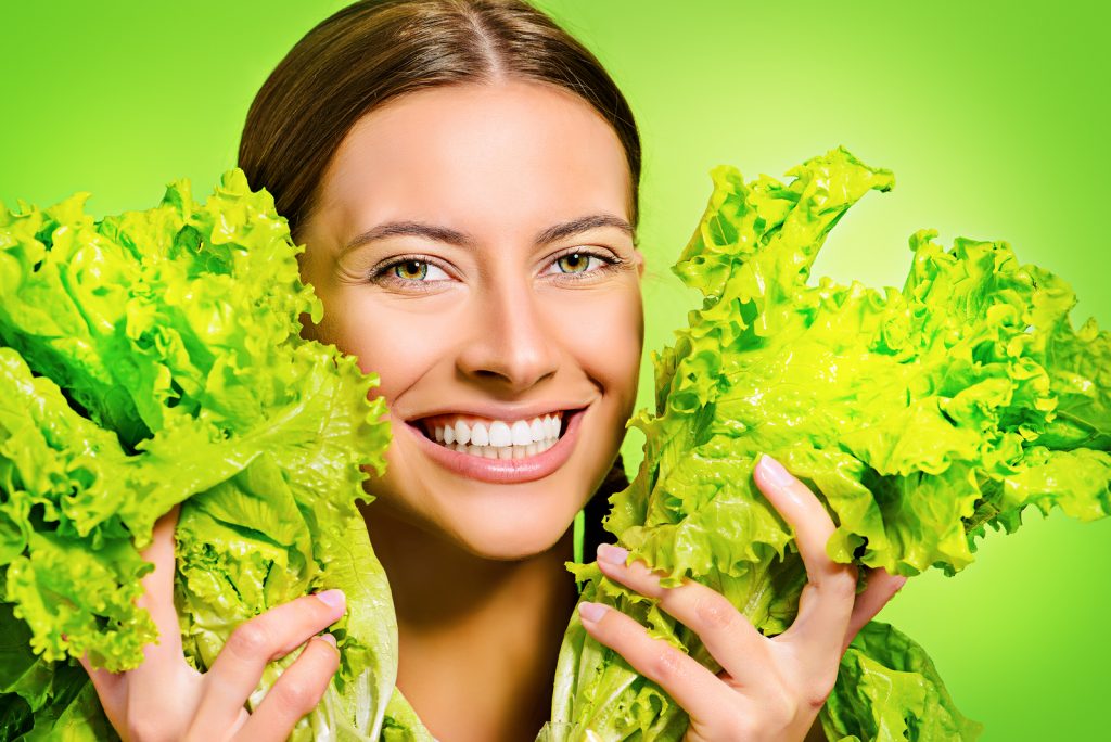 Pretty cheerful young woman posing with fresh green lettuce leav